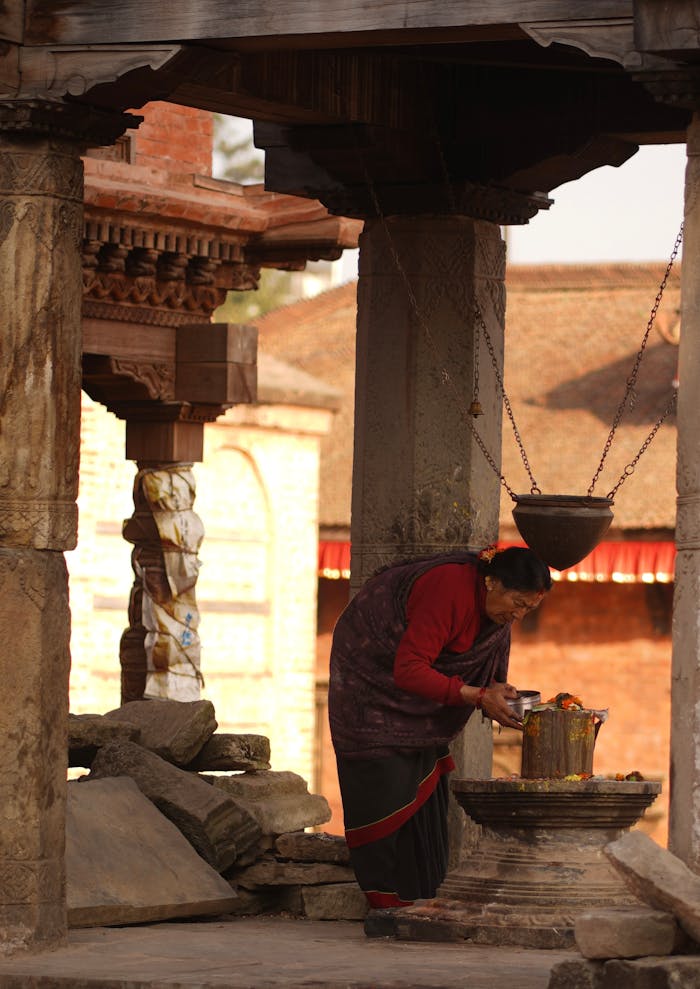 A woman performing a prayer ritual with a candle at a historic temple in Bhaktapur, Nepal.