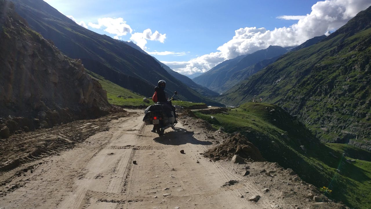 A solo motorcyclist navigates a rugged mountain road under a clear blue sky.