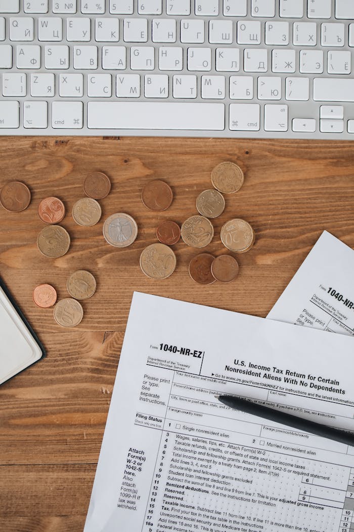 Top view of tax forms, coins on a wooden desk with a keyboard.